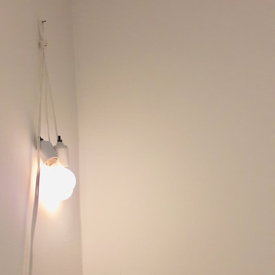 This is an untitled piece by conceptual artist Felix Gonzalez-Torres. It is a pair of bare lightbulbs hanging from their cord in the corner of a room.